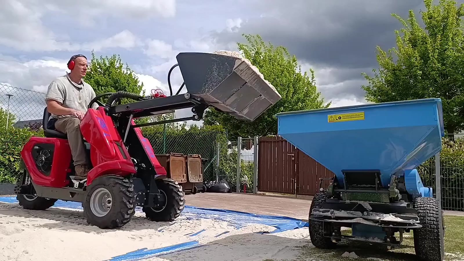 Mini nakladač Heracles H130 při přepravě písku a plnění rozmetadla
